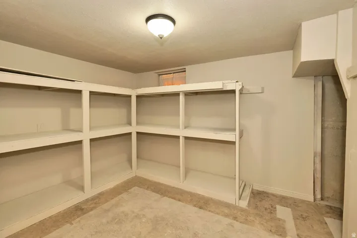 Utility room featuring extensive built-in shelving, a concrete floor, a ceiling-mounted light fixture, and a small window