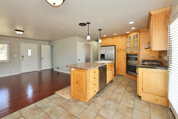 Kitchen featuring light wood cabinetry, stainless steel appliances, a tile backsplash, and a central island with a stone-finish countertop