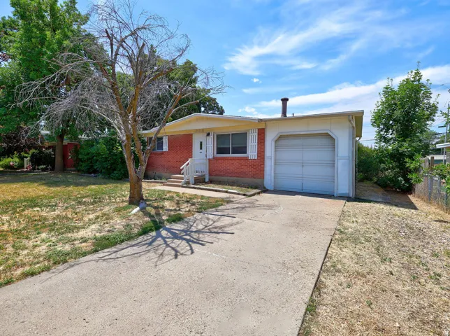 Brick ranch-style exterior featuring a concrete driveway, attached garage, white entry door, and white window shutters