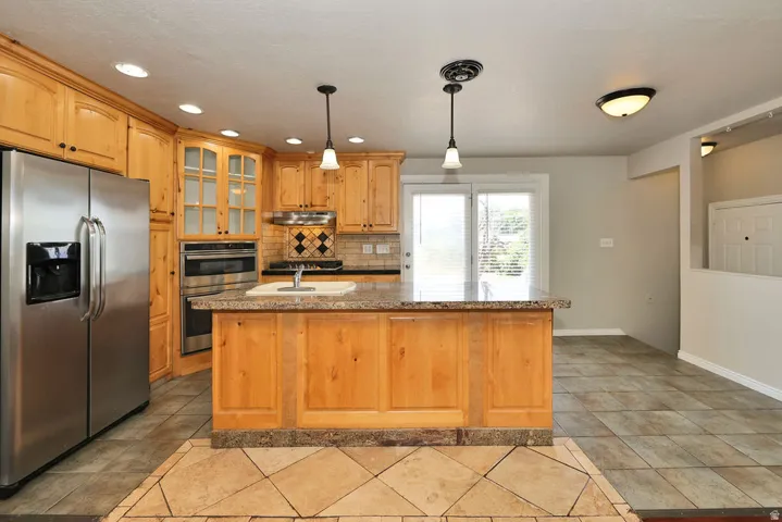 Kitchen featuring wood cabinetry, stainless steel appliances, and a granite-finish island with integrated sink