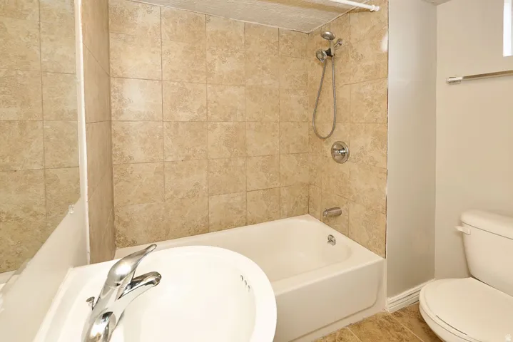 Bathroom featuring a full-size bathtub with beige tile surround, chrome shower fixtures, white vanity sink with chrome faucet, and a toilet