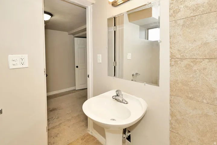 Pedestal sink with chrome faucet, complemented by a wall-mounted mirror and vanity light fixture