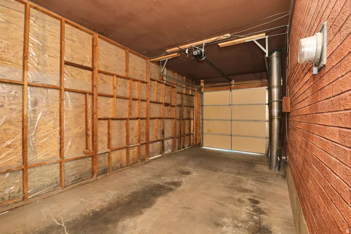 Garage space featuring a single insulated garage door, concrete flooring, wood-framed unfinished walls, and a brick exterior wall
