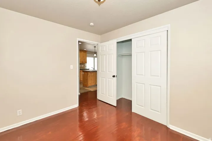 Bedroom featuring wood-finish flooring, neutral wall paint, white trim, and a bi-fold closet with shelving and hanging rod