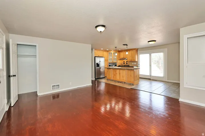 Hardwood-finish flooring extending into an open-concept kitchen featuring light wood cabinetry, a breakfast bar with pendant lighting, and stainless steel appliances