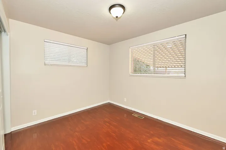 Neutral-toned walls complement wood-finish flooring in this room featuring two windows with horizontal blinds
