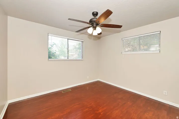 Spacious room featuring wood-finish flooring, two windows with horizontal blinds, a ceiling fan with light kit, and neutral wall paint