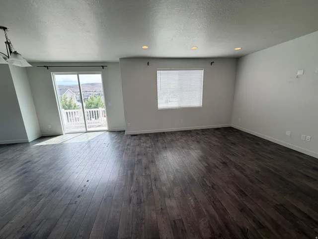 Spacious interior featuring wood-finish flooring, recessed lighting, and a glass sliding door opening to a white railing balcony
