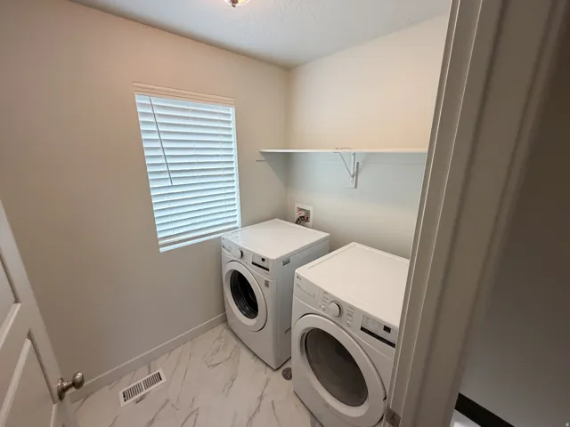 Utility room featuring a window with blinds, a wall-mounted shelf, and wood-finish flooring