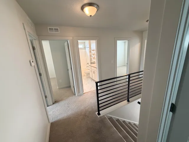 Carpeted hallway with a modern black metal horizontal railing overlooking a carpeted staircase