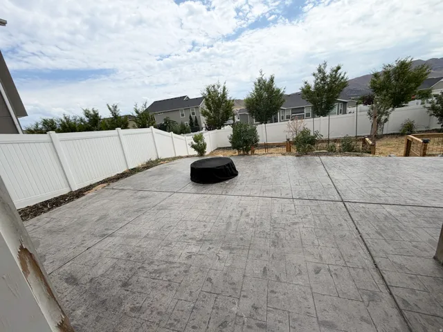 Expansive stamped concrete patio featuring a white vinyl privacy fence and mature landscaping elements
