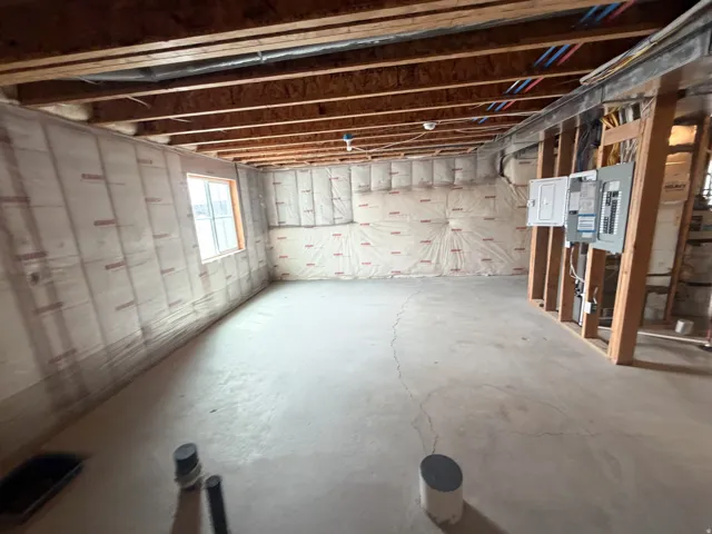 Unfinished basement featuring exposed wood joists, insulated walls, an egress window, and visible electrical panels