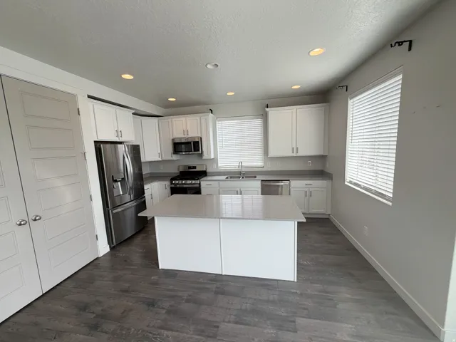 Modern kitchen featuring an expansive center island, stainless steel appliances, white cabinetry, recessed lighting, and wood-finish flooring