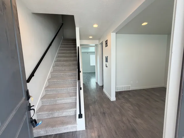 Inviting entryway featuring wood-finish flooring, a carpeted staircase with a black handrail, recessed lighting, and a neutral color palette