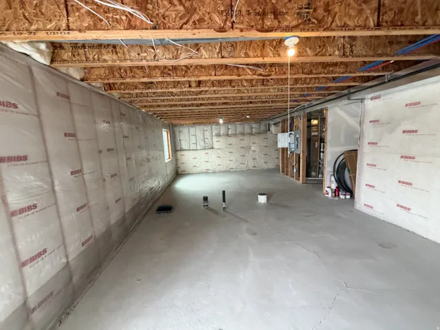 Unfinished basement featuring exposed wood joists, concrete flooring, insulated perimeter walls, a visible electrical panel, and PEX plumbing