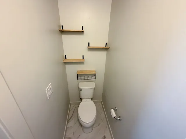 Powder room featuring a toilet with an overhead wood-finish shelf and three additional wood-finish floating shelves