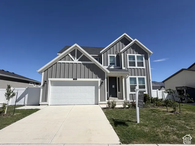 Two-story exterior with board and batten siding, attached garage, concrete driveway, and front lawn