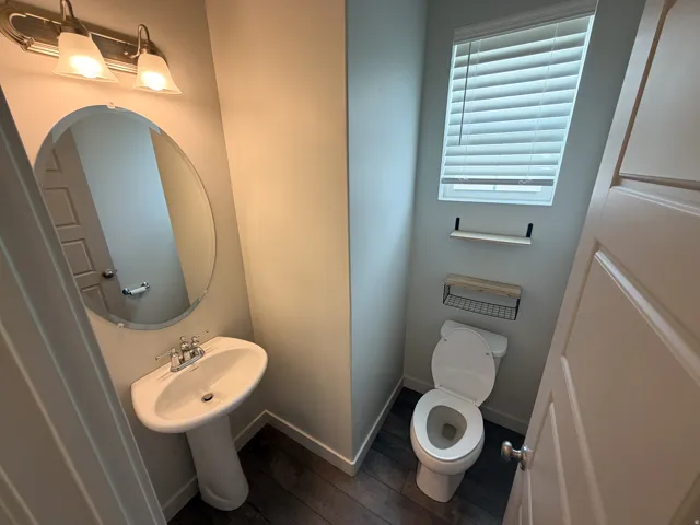Pedestal sink with chrome faucet, oval mirror, and overhead vanity lighting