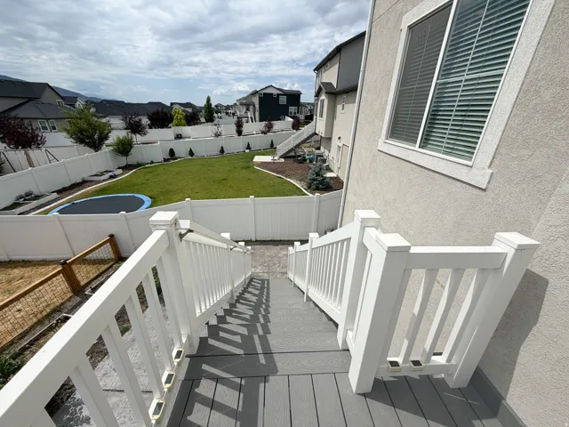 Expansive backyard featuring a manicured lawn, white vinyl fencing, and mature landscaping