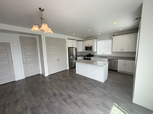 Kitchen area featuring wood-finish flooring, white cabinetry, a central island, and stainless steel appliances