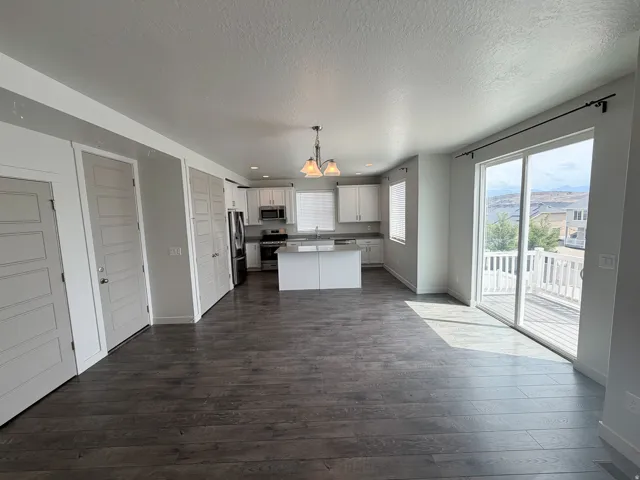 Open-concept living area featuring wood-finish flooring, white cabinetry, a kitchen island, stainless steel appliances, and sliding glass doors to a deck with white railings