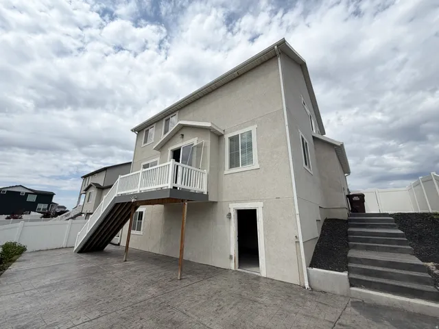Rear exterior featuring a stucco finish, a second-story balcony with white railing, and a stamped concrete patio