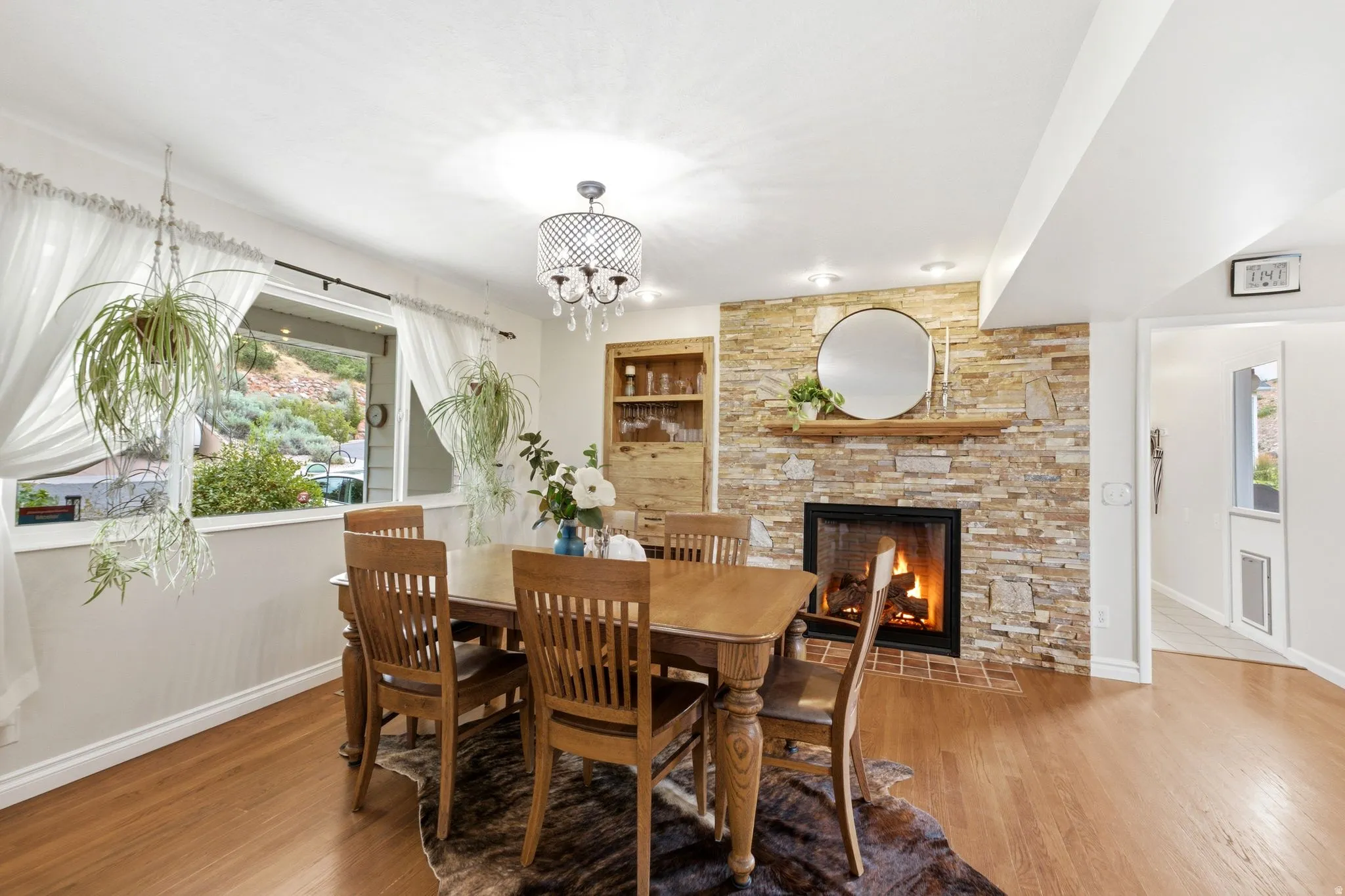Dining area featuring a stone accent wall with a built-in fireplace, wood-finish flooring, a contemporary chandelier, and recessed lighting