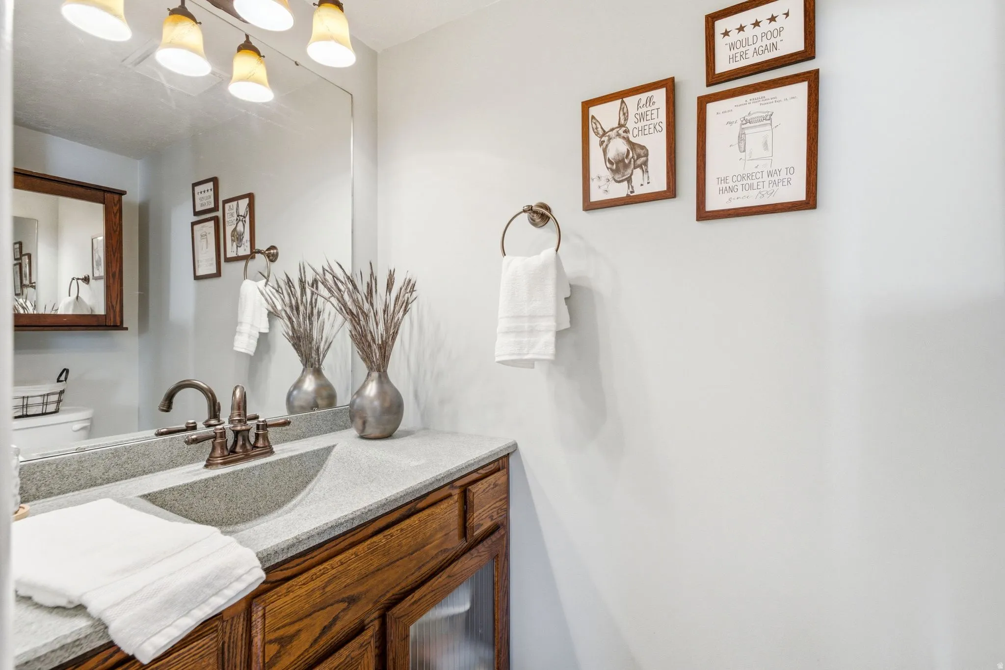 Vanity featuring wood-finish cabinetry, a light-toned countertop with integrated sink, and an oil-rubbed bronze faucet