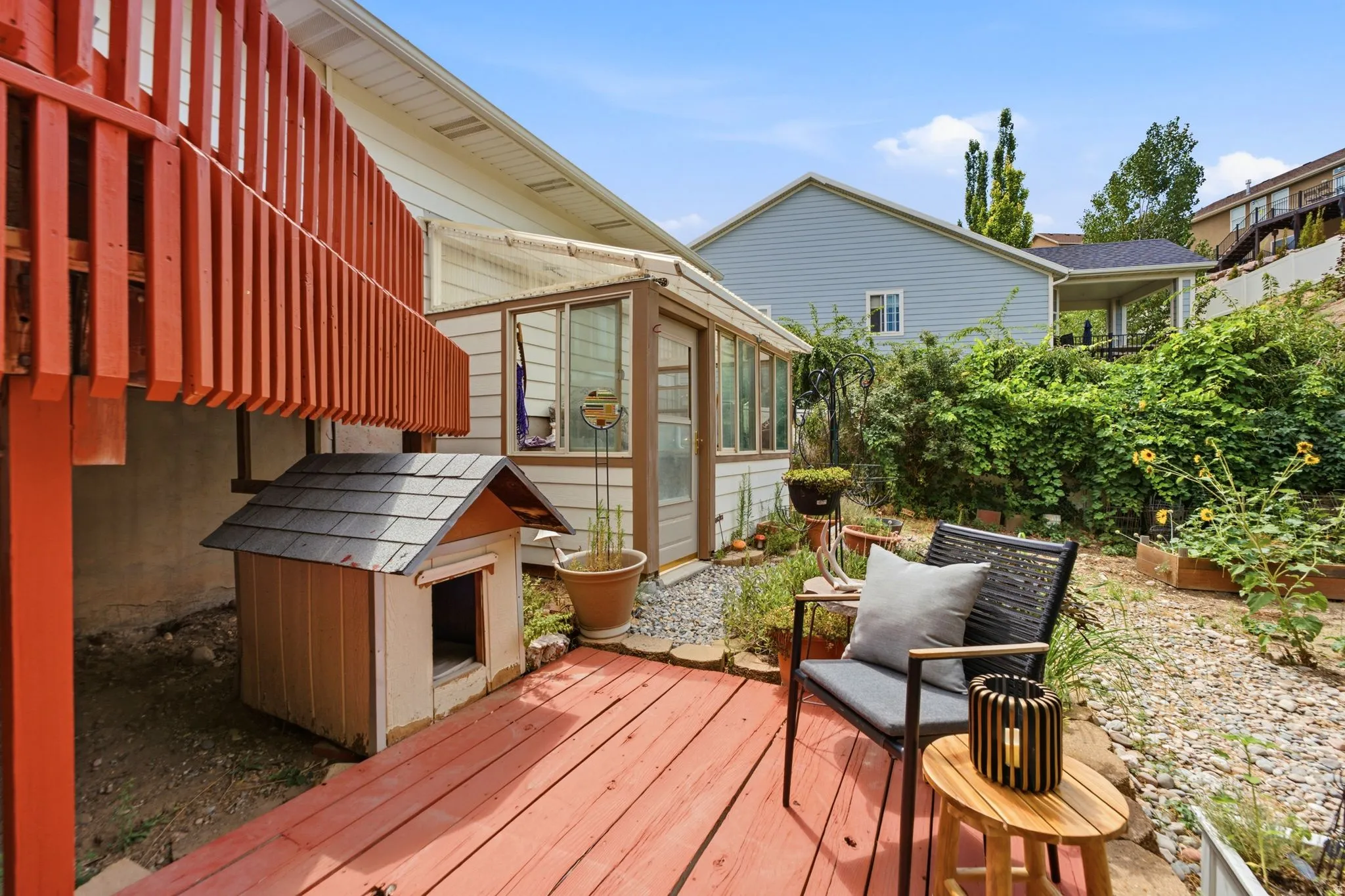 Red-stained wood deck featuring a sunroom addition with multiple windows