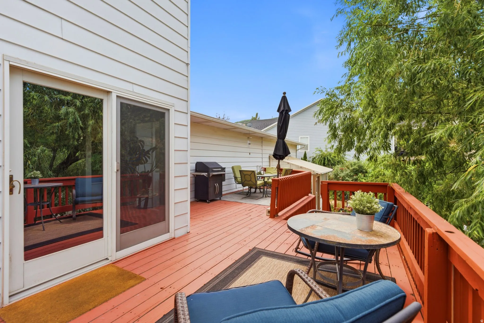 Expansive wood deck featuring a rich red finish, a safety railing, and direct access through a sliding glass door