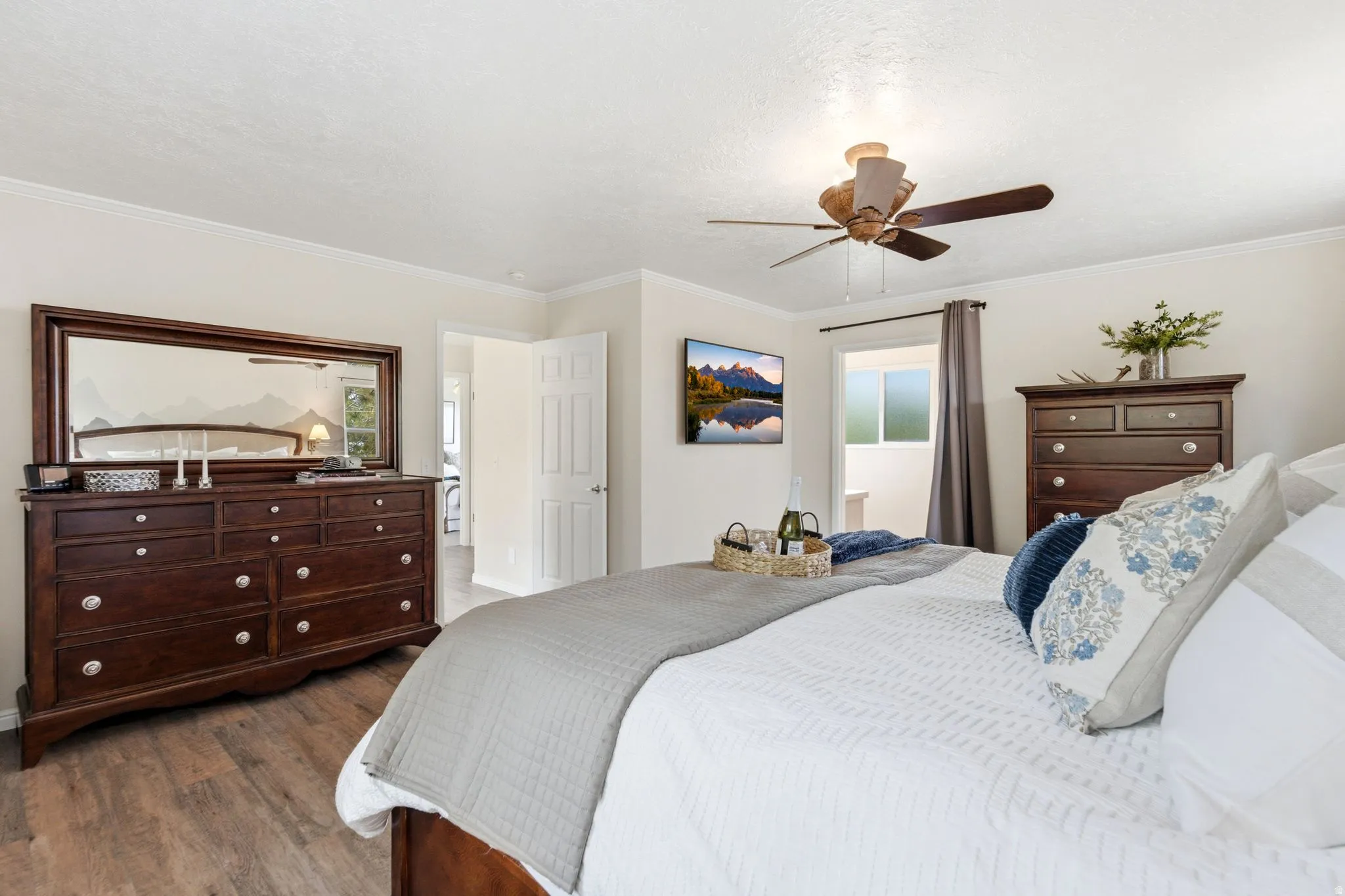 Spacious bedroom featuring wood-finish flooring, a ceiling fan with integrated lighting, and crown molding