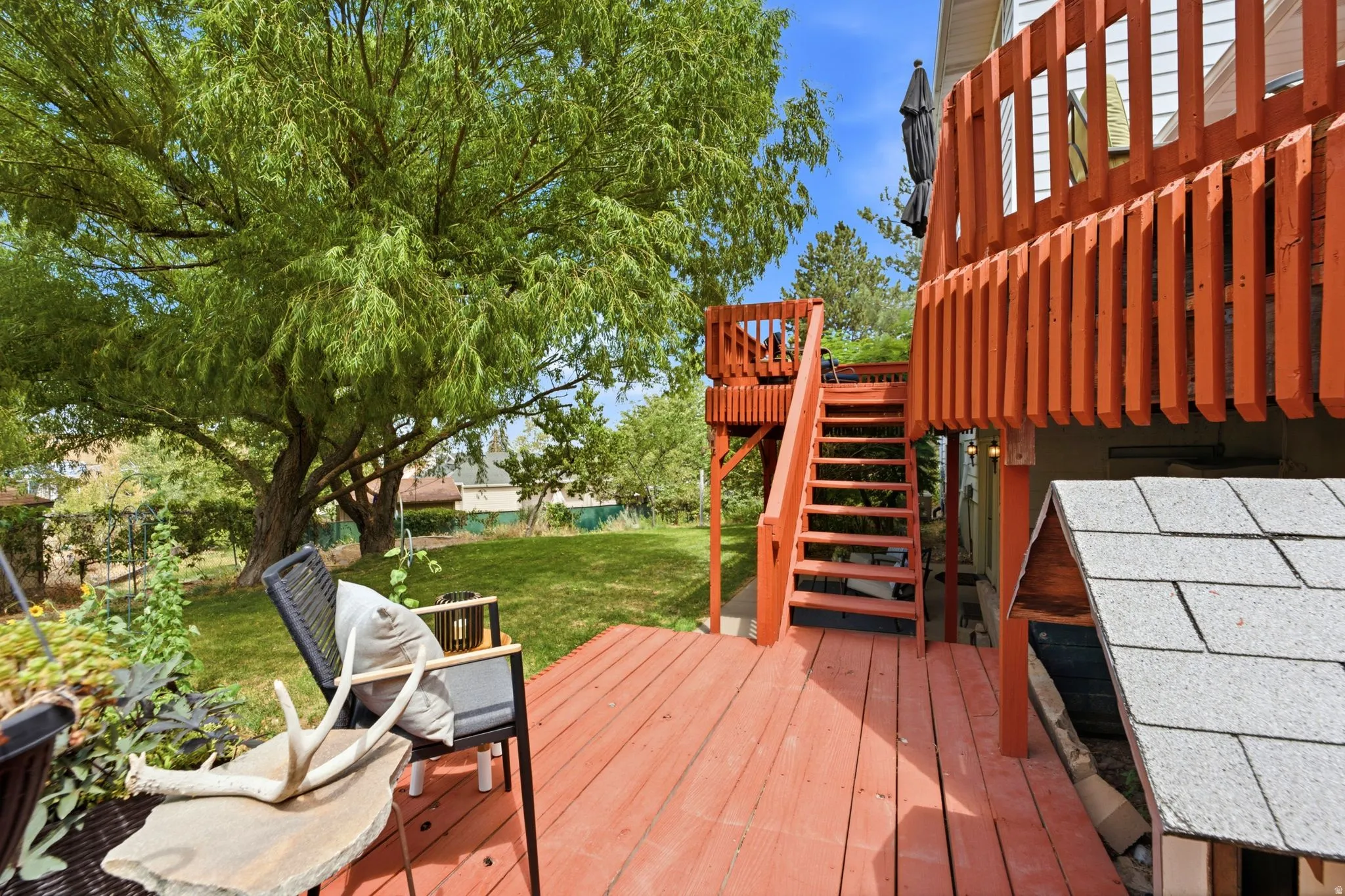 Multi-level wooden deck featuring a staircase and railing, overlooking a lush green lawn with a mature tree