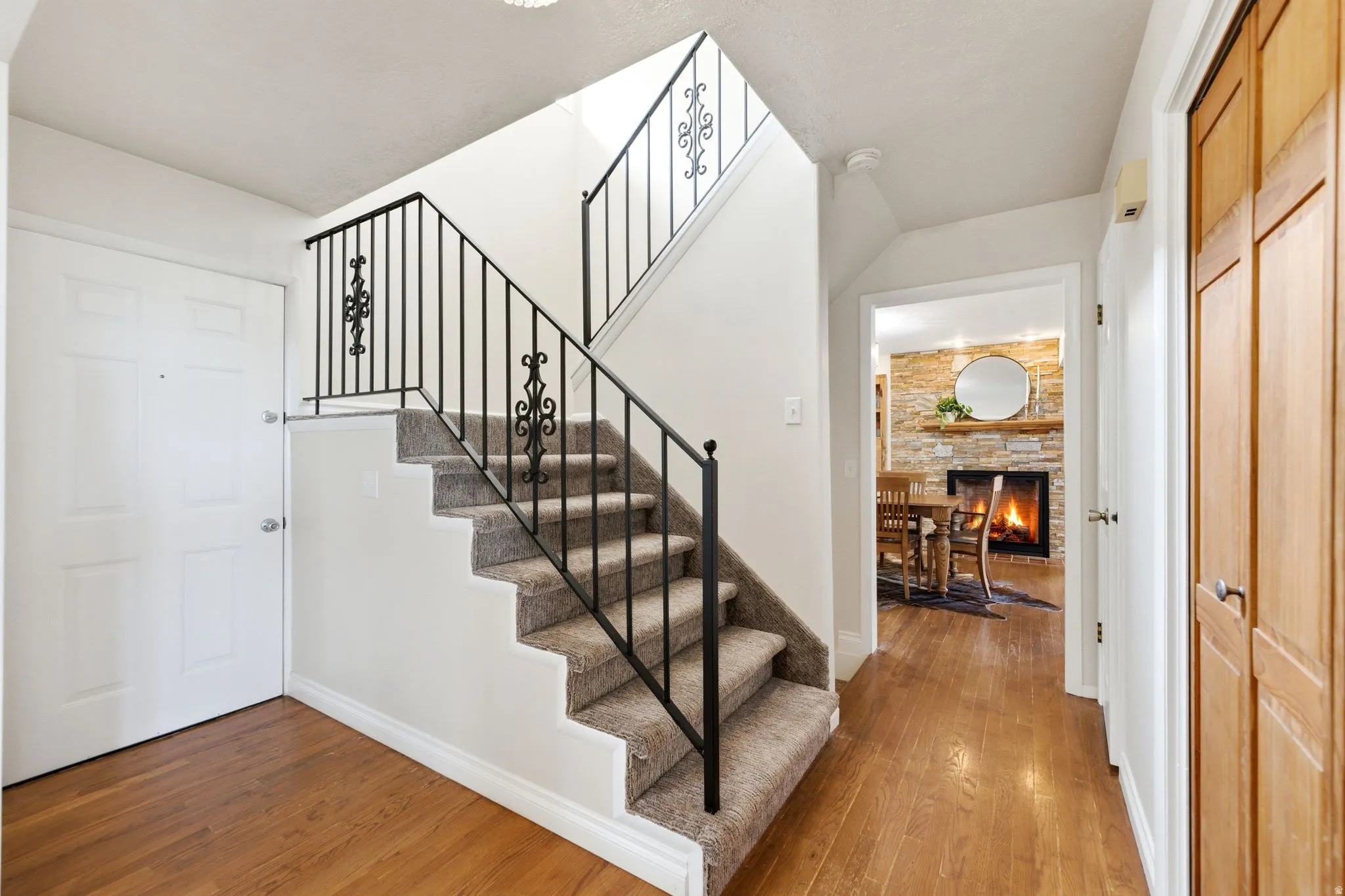 Entryway featuring wood-finish flooring, a carpeted staircase with ornate wrought iron railings, and a coat closet with natural wood paneled doors