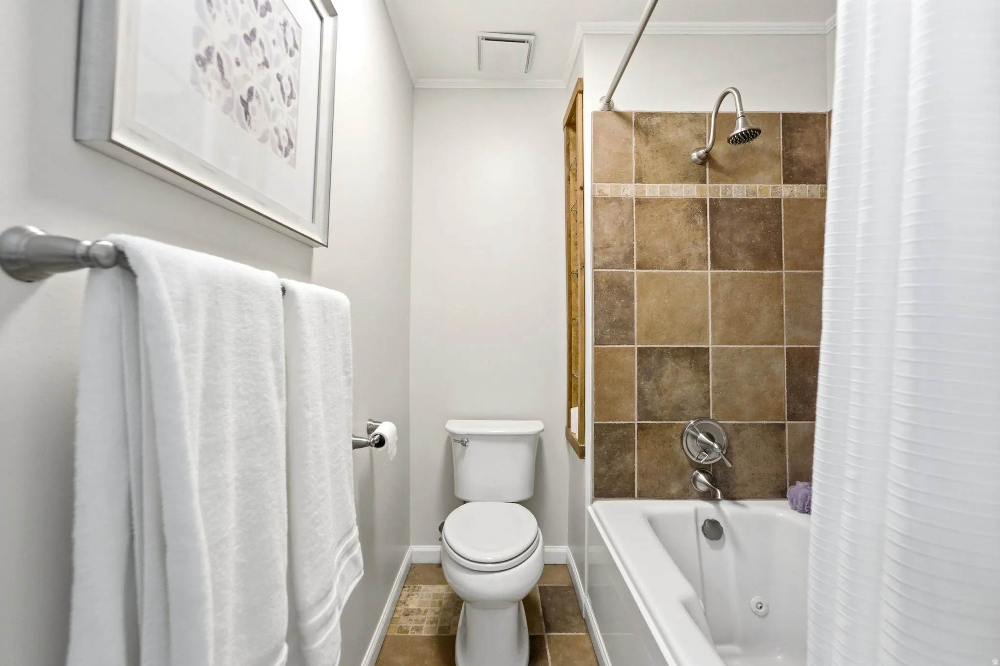 Bathroom featuring a tiled tub/shower combination with chrome fixtures, a white toilet, and coordinating floor tiles