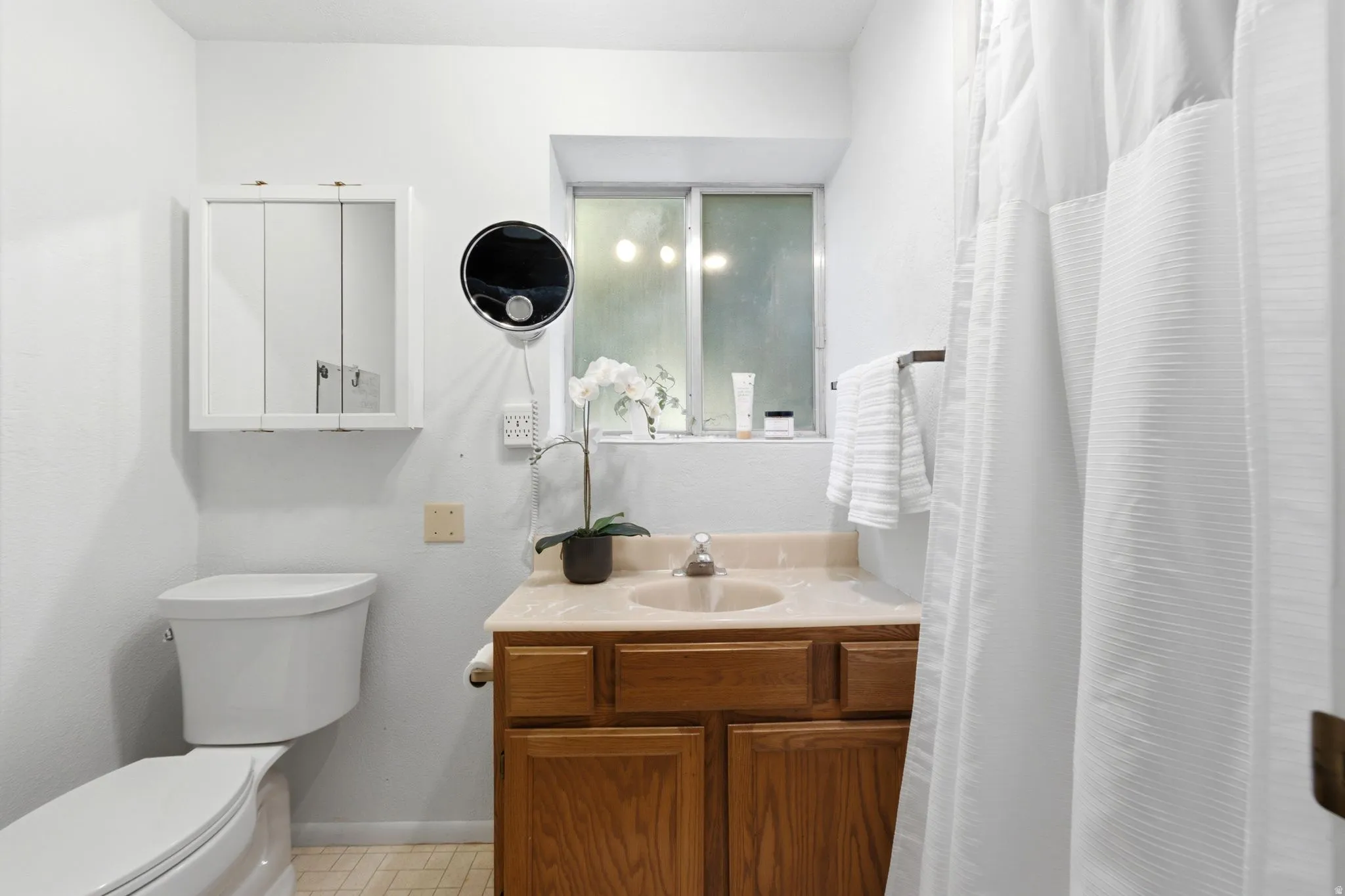 Bathroom featuring a wood-finish vanity with an integrated sink and light-toned countertop, a white medicine cabinet, and a window with frosted glass