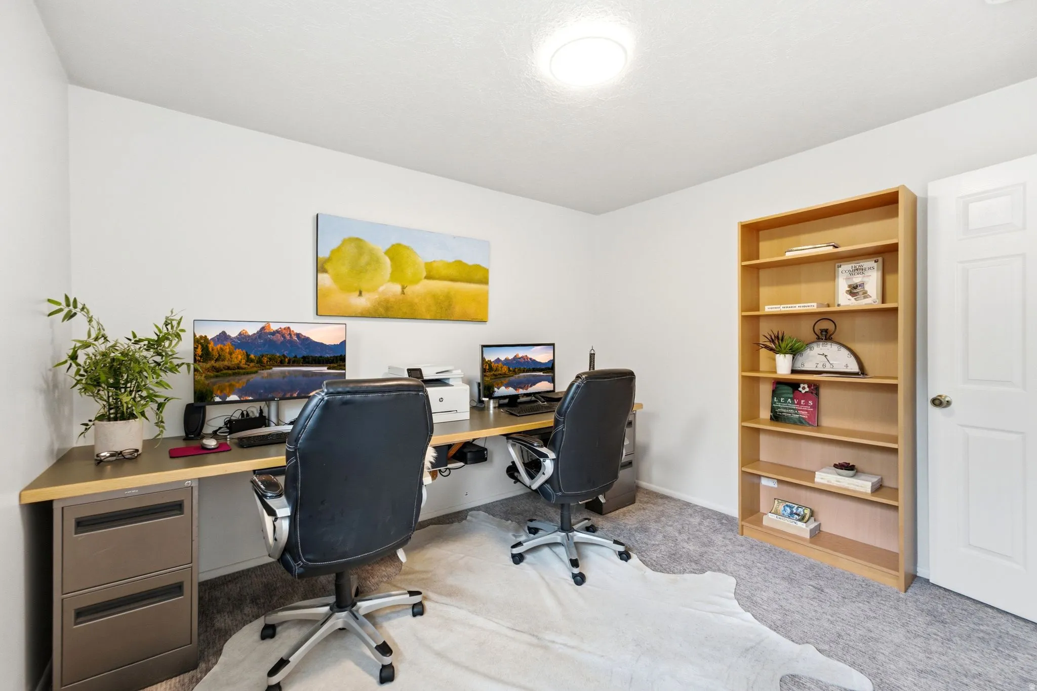 Dedicated office space featuring a light wood-finish desk with metal filing cabinets, neutral wall paint, and a built-in light wood-finish shelving unit