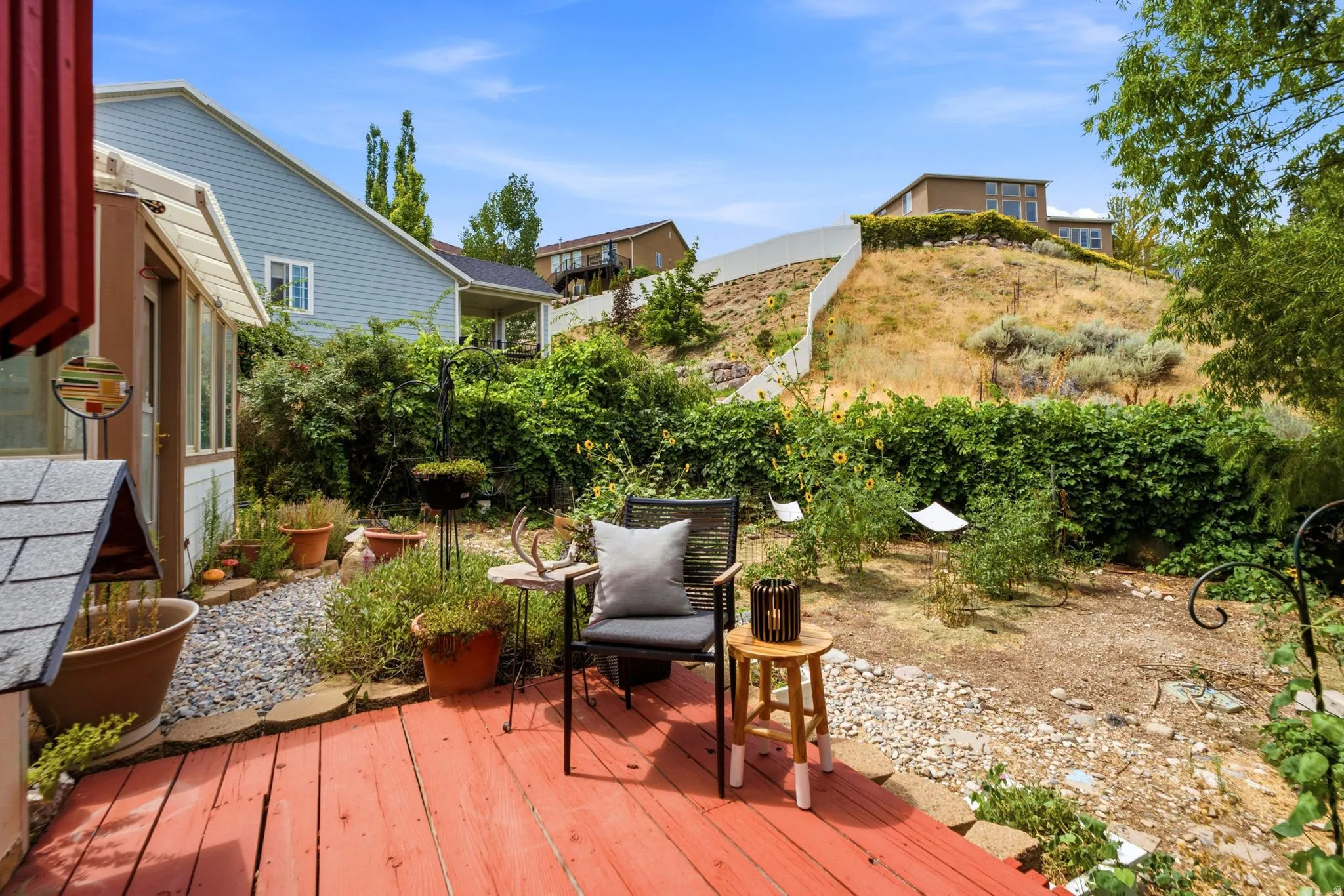 Red wood deck surface with a gravel pathway, surrounded by varied plantings and greenery