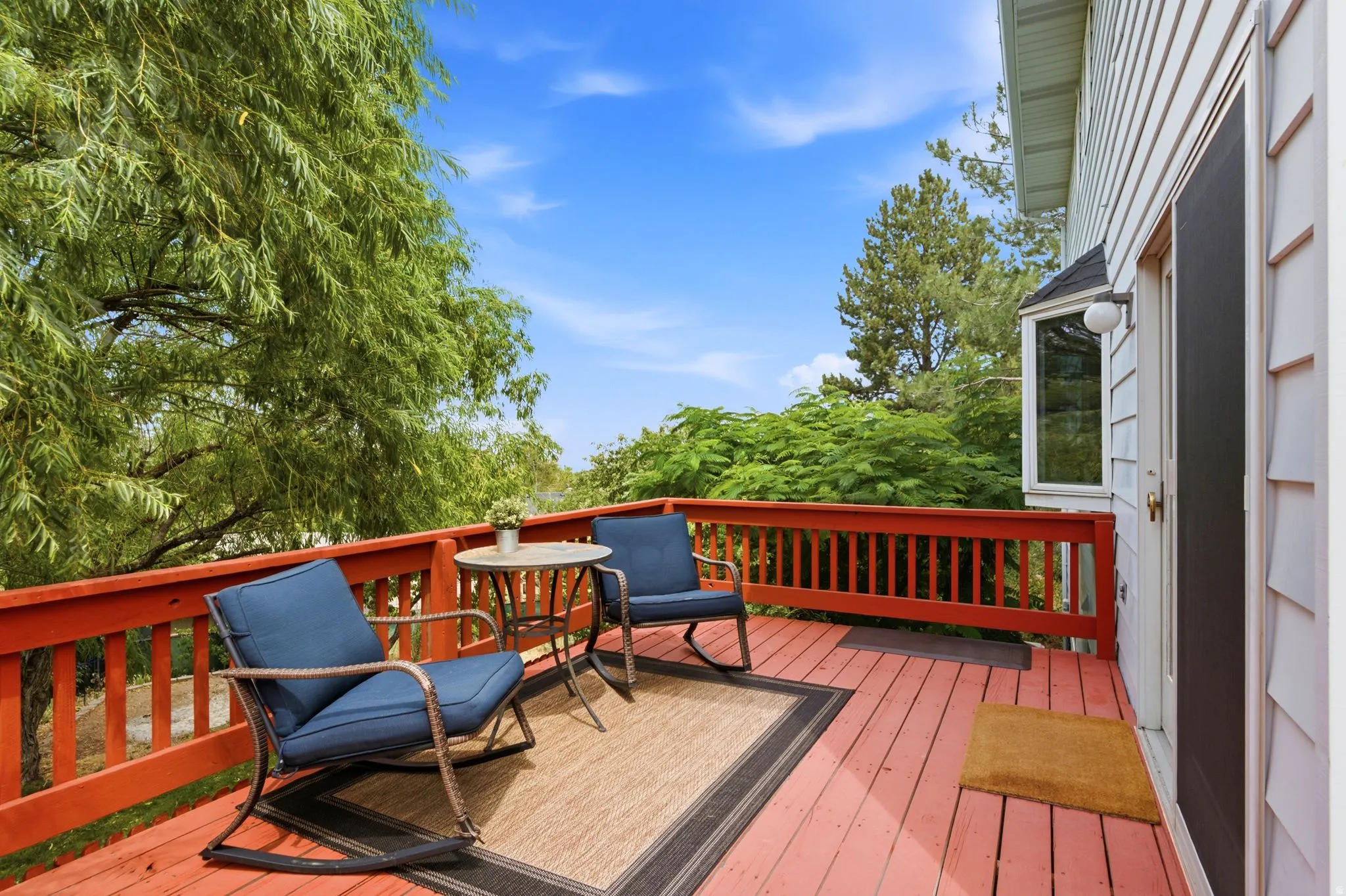 Expansive wooden deck with a red stain, surrounded by mature trees