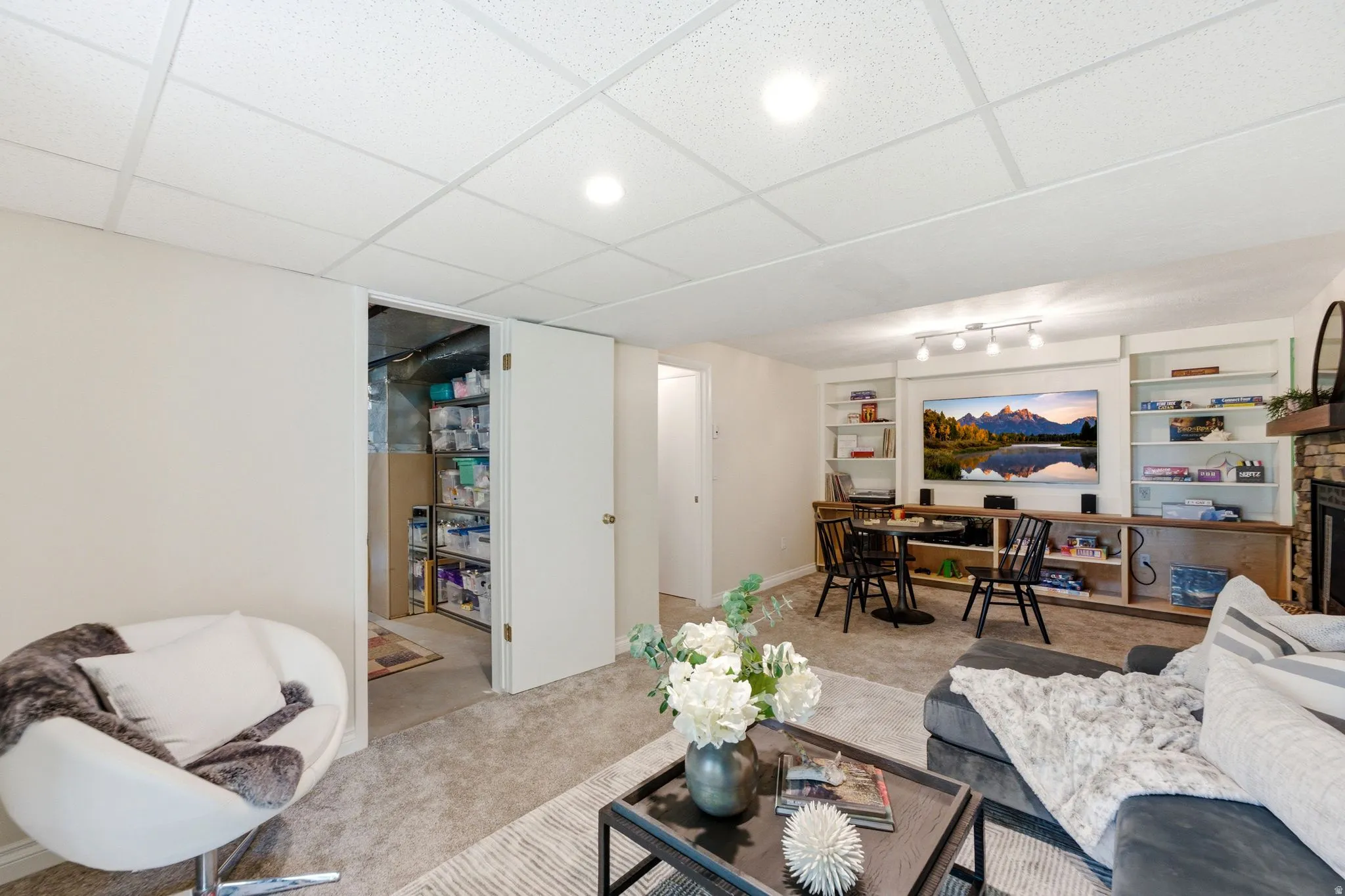 Finished basement entertainment area featuring integrated shelving, built-in media console, recessed lighting, and a stone-faced fireplace