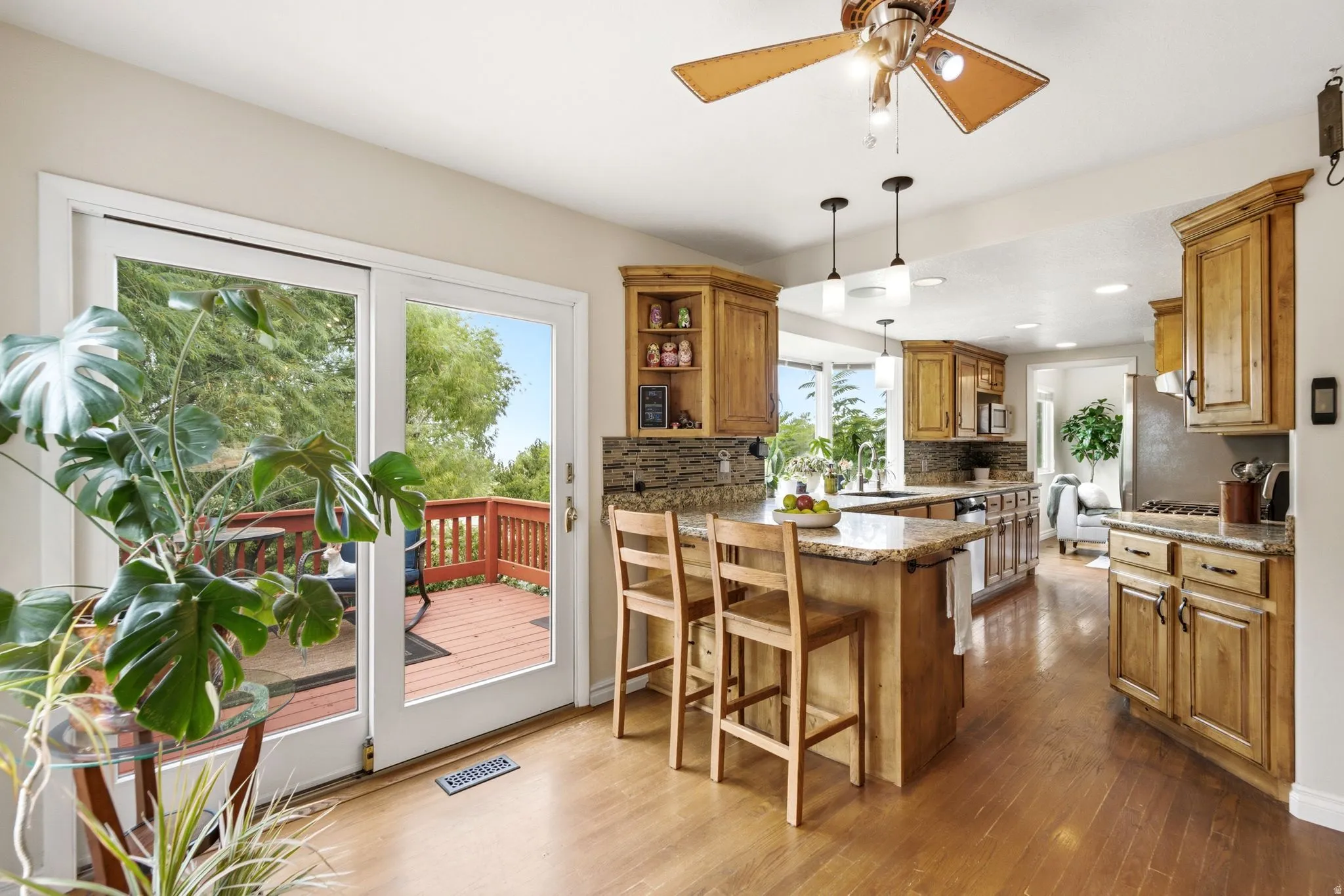 Spacious kitchen featuring natural wood cabinetry, granite countertops, stone tile backsplash, and wood-finish flooring