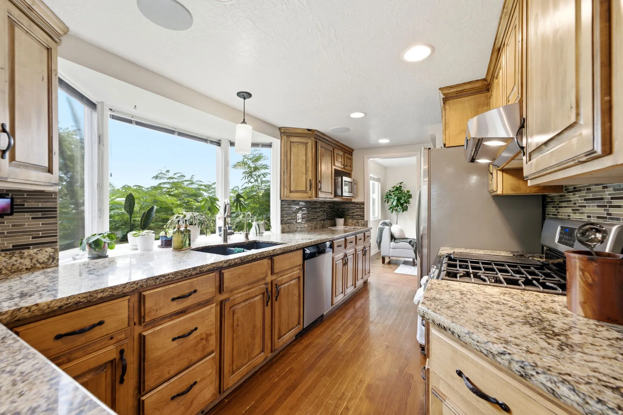 Kitchen featuring a large bay window, wood-finish flooring, granite countertops, and stainless steel appliances