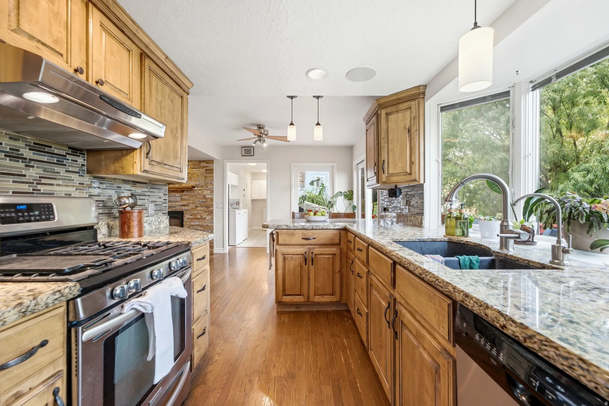 Kitchen featuring granite countertops, wood-finish flooring, stainless steel appliances, a tile backsplash, and a bay window