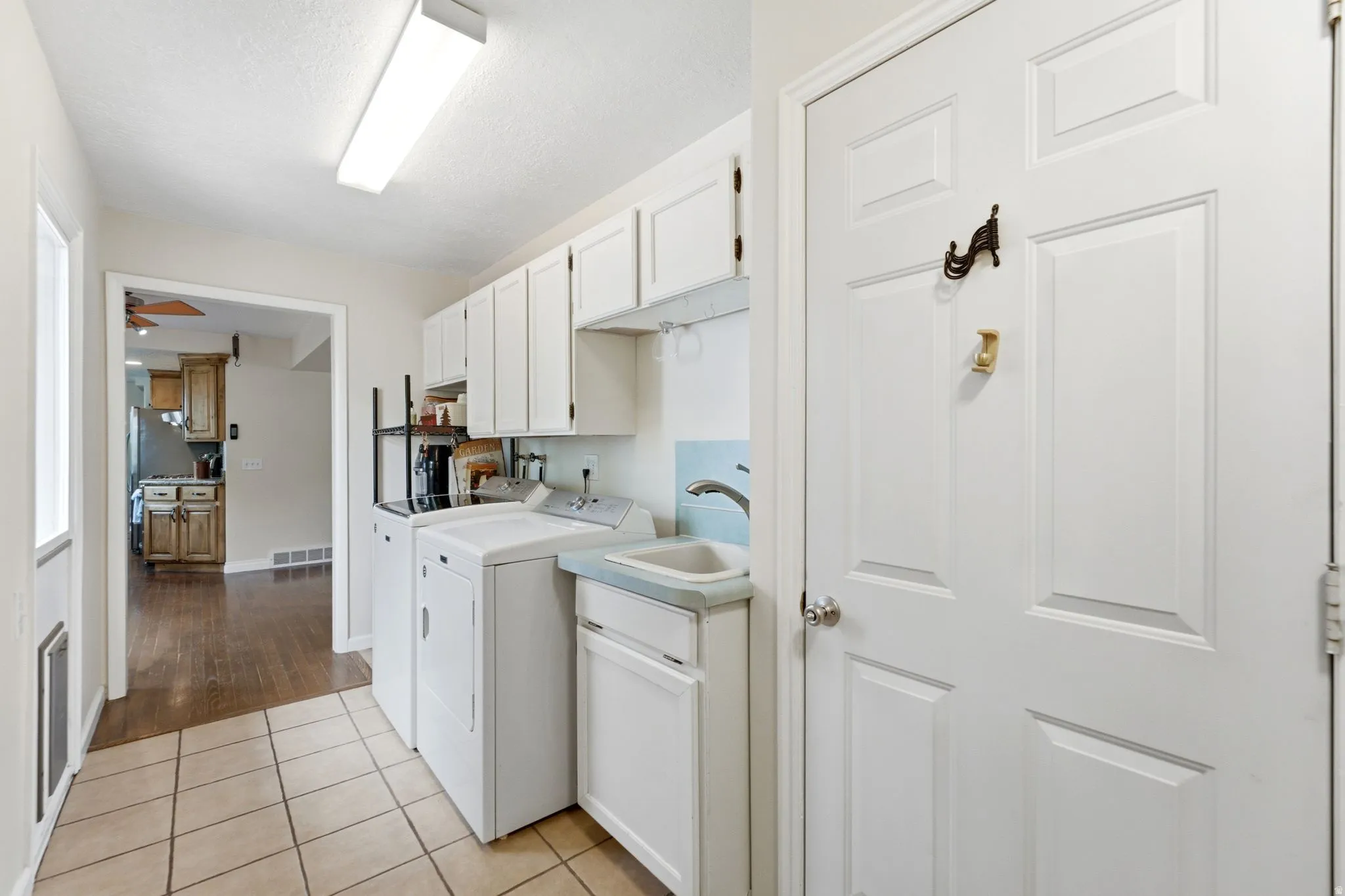 Laundry area with tile flooring, white cabinetry, utility sink, and overhead lighting
