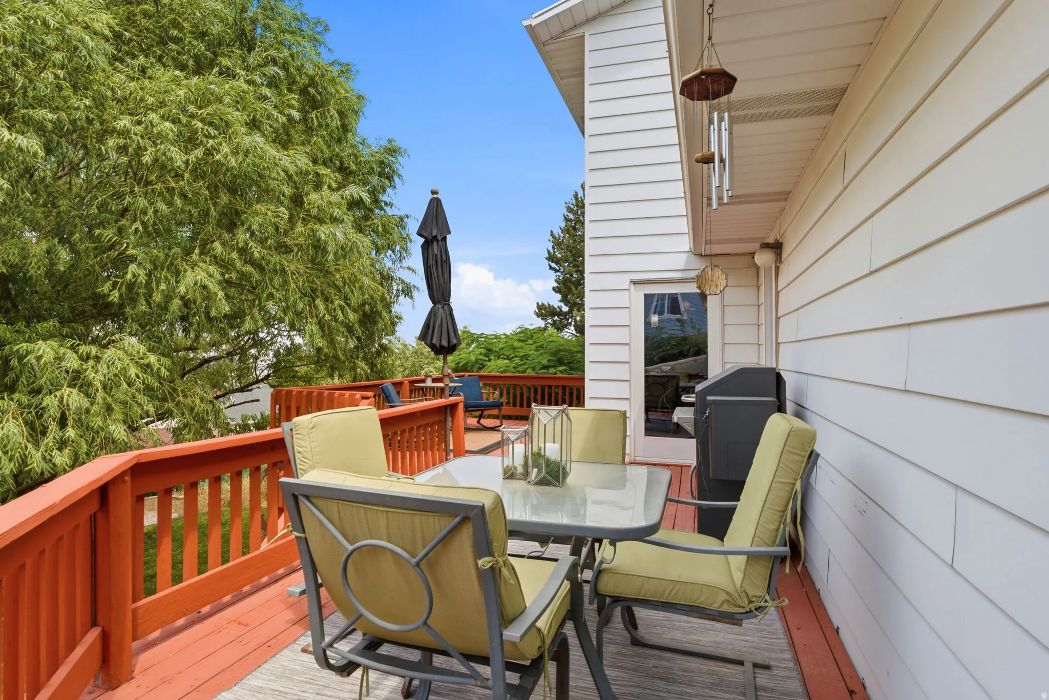 Expansive wood deck with a red-stained railing, white siding exterior, and mature tree canopy