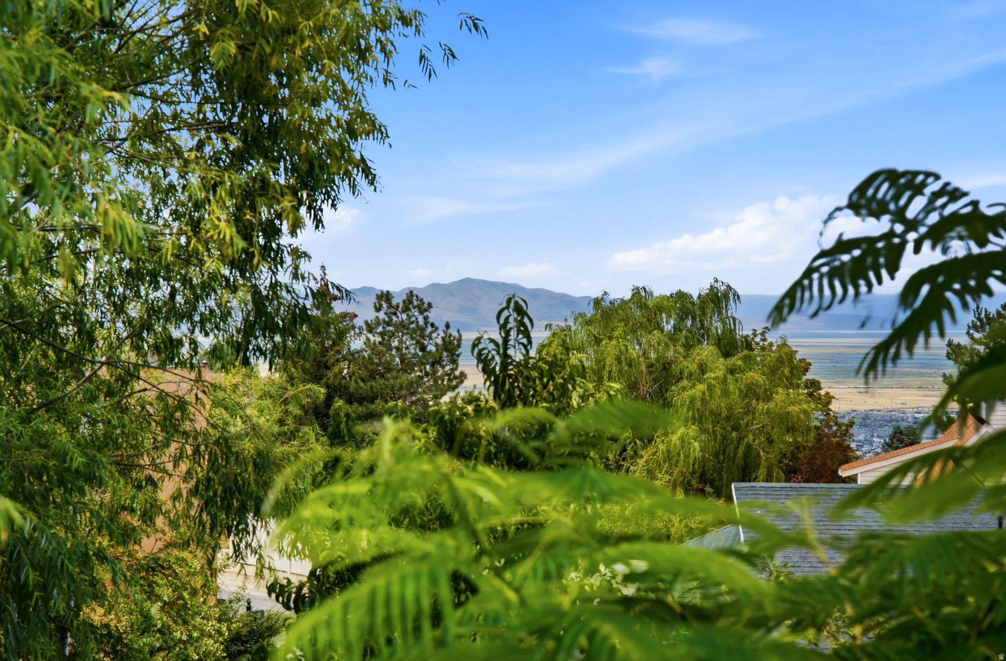 Expansive natural landscape with distant mountains, a large body of water, and surrounding greenery under a bright blue sky