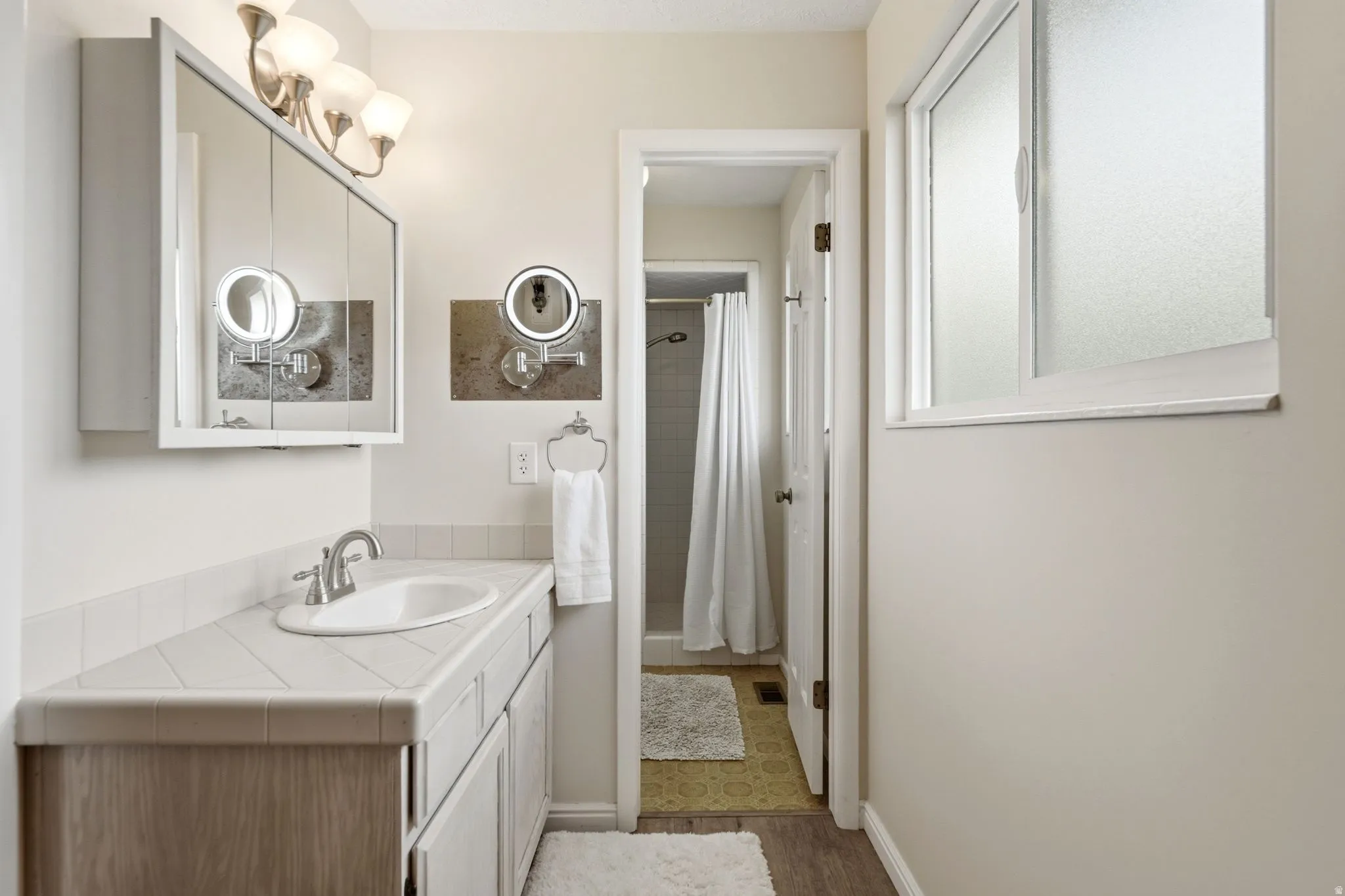 Bathroom vanity featuring a single basin sink, tile countertop, and wood-finish cabinetry