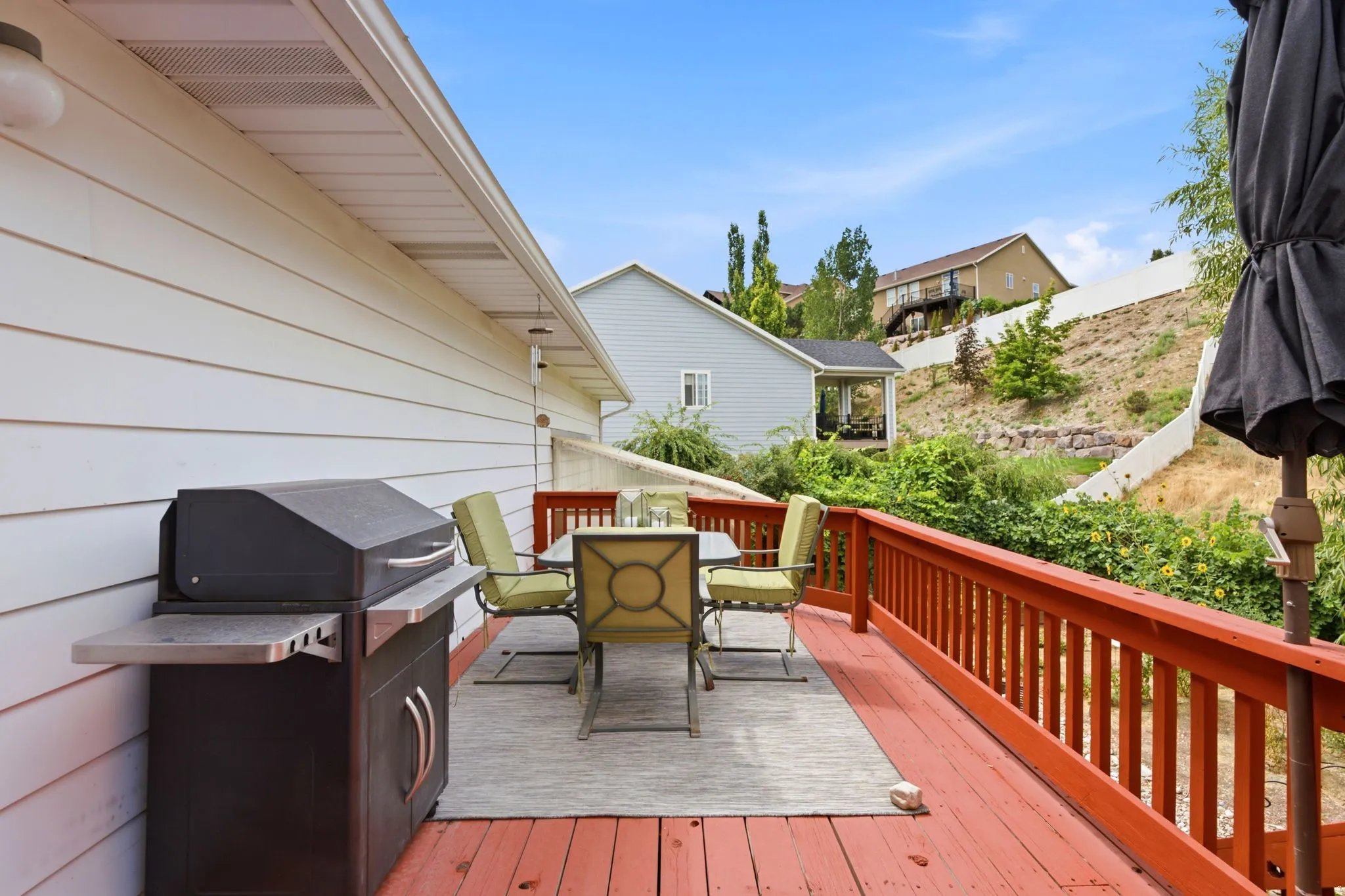 Expansive wood deck with a red-stained railing, featuring a designated outdoor dining area and white vinyl siding
