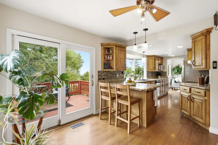 Spacious kitchen featuring natural wood cabinetry, granite countertops, stone tile backsplash, and wood-finish flooring