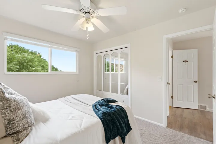 Bright room featuring a window with green tree scenery, a ceiling fan, mirrored closet doors, and light neutral wall paint