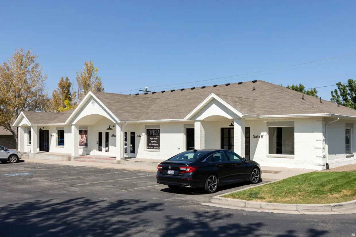 Single-story commercial building featuring a light-colored brick exterior, a dark shingle roof, and multiple tenant suites